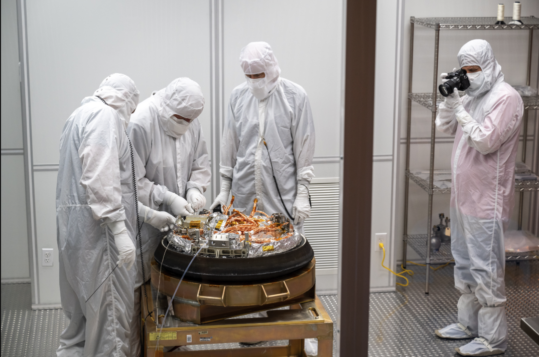 Four people in white suits examine sample